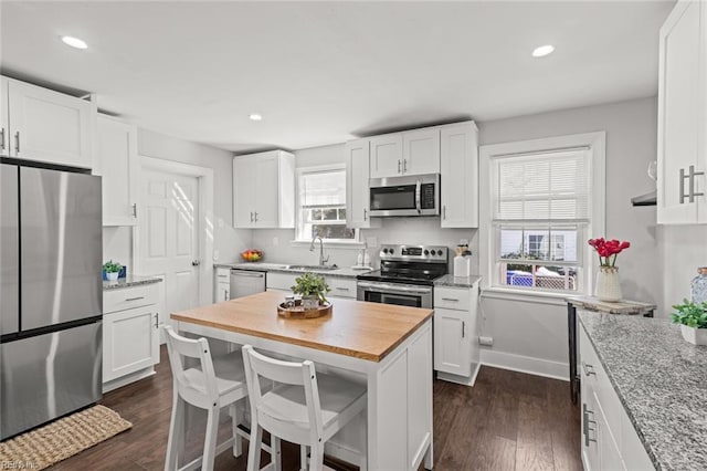 kitchen featuring appliances with stainless steel finishes, light stone countertops, a center island, sink, and white cabinetry