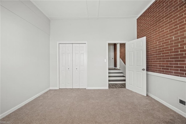 unfurnished bedroom featuring carpet floors, a closet, and brick wall