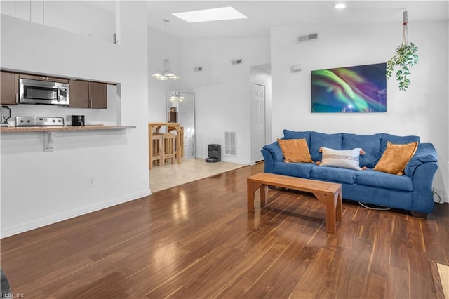 living room featuring dark hardwood / wood-style flooring, a skylight, and high vaulted ceiling