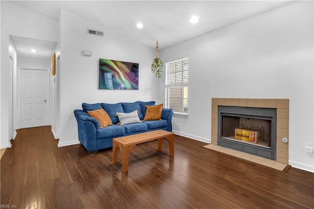 living room featuring a tiled fireplace, lofted ceiling, and hardwood / wood-style floors