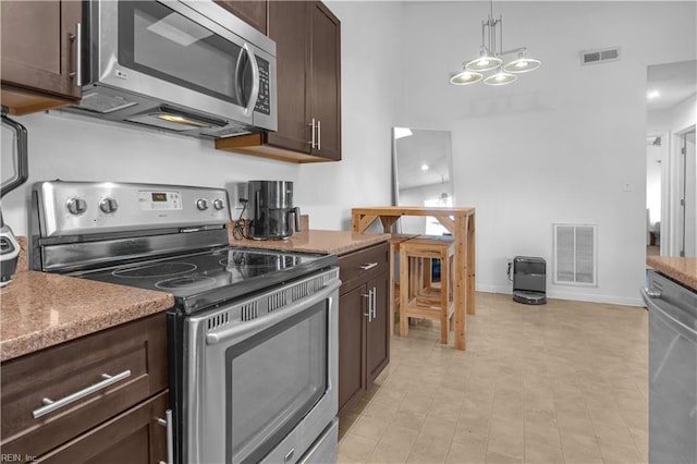 kitchen with hanging light fixtures, light stone countertops, appliances with stainless steel finishes, and dark brown cabinetry