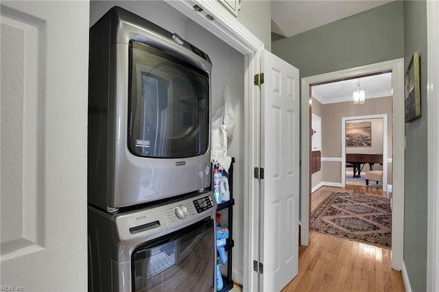 clothes washing area with crown molding, stacked washer / drying machine, light wood-style flooring, laundry area, and baseboards