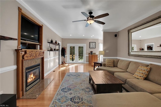 living room with light wood-style flooring, a premium fireplace, crown molding, and french doors