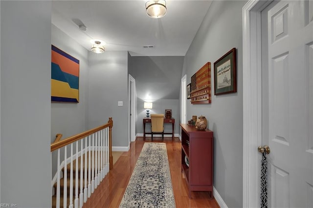 hall featuring light wood-style floors, baseboards, visible vents, and an upstairs landing