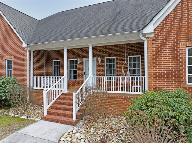 view of exterior entry featuring brick siding, a porch, and roof with shingles