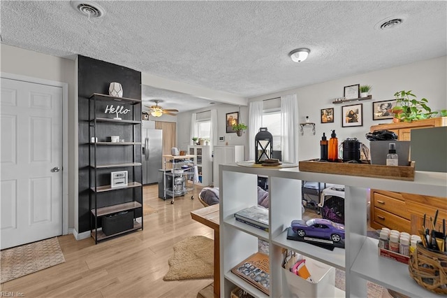 interior space featuring light wood-type flooring, a textured ceiling, stainless steel fridge with ice dispenser, and ceiling fan