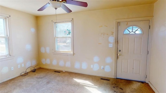 foyer entrance featuring a ceiling fan, light colored carpet, visible vents, and baseboards