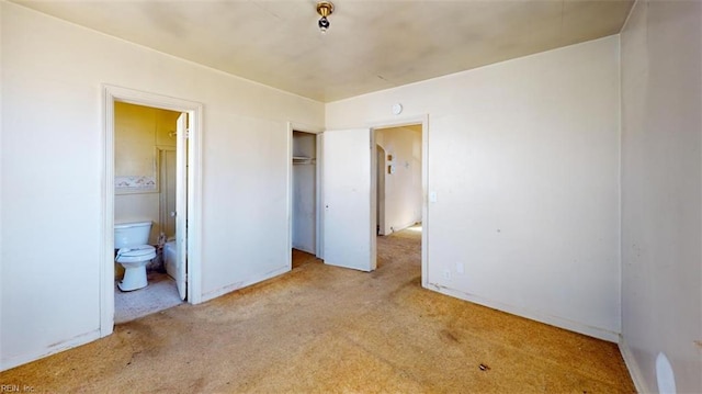 unfurnished bedroom with a closet, light colored carpet, and connected bathroom