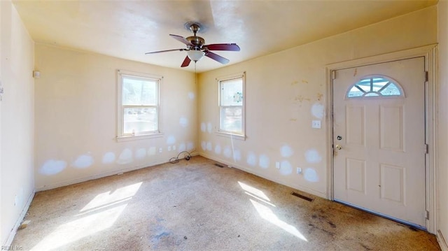 foyer entrance featuring a ceiling fan, light colored carpet, visible vents, and baseboards