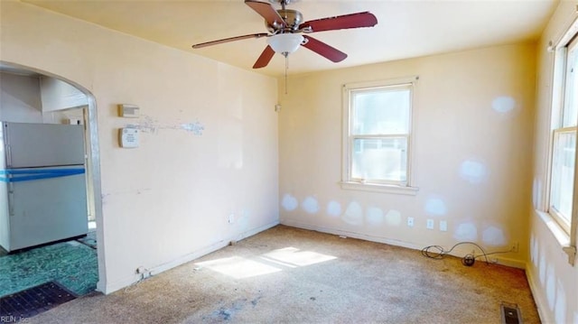 carpeted spare room with a ceiling fan, arched walkways, visible vents, and baseboards