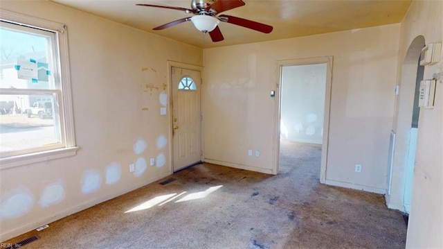 foyer entrance with arched walkways, visible vents, light carpet, ceiling fan, and baseboards