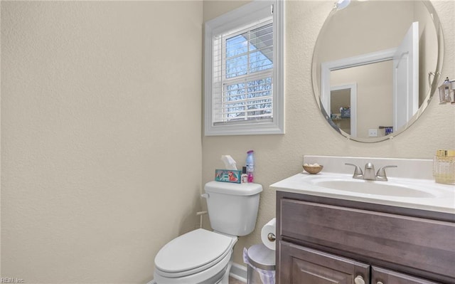 half bath featuring a textured wall, baseboards, vanity, and toilet
