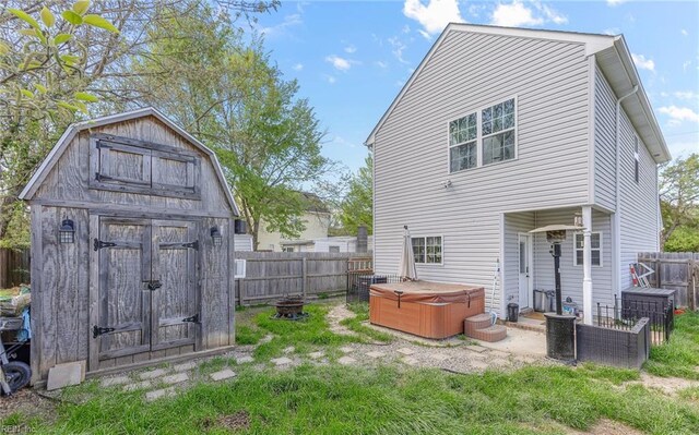 rear view of house featuring a storage unit, a fenced backyard, an outbuilding, and a hot tub