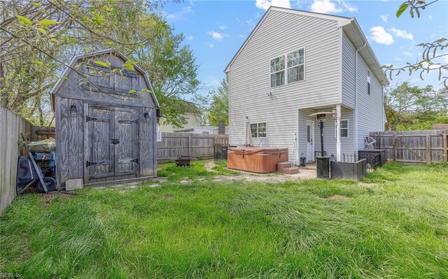 rear view of property featuring a storage shed, a fenced backyard, a yard, and a hot tub