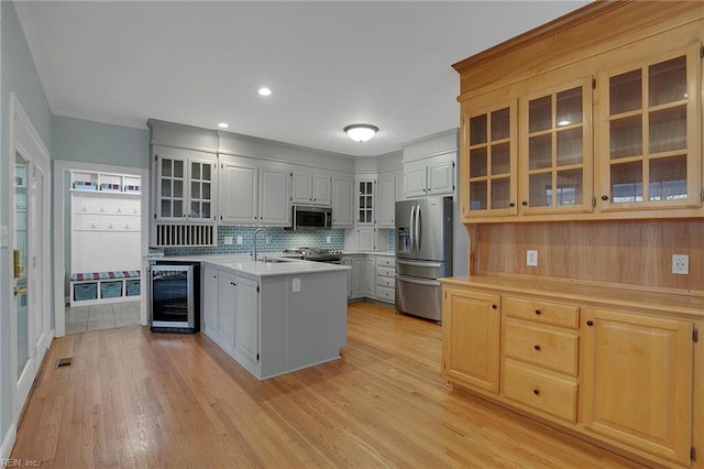 kitchen featuring appliances with stainless steel finishes, light wood-type flooring, tasteful backsplash, and beverage cooler