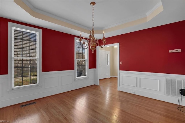 unfurnished dining area featuring a tray ceiling, ornamental molding, hardwood / wood-style floors, and a chandelier