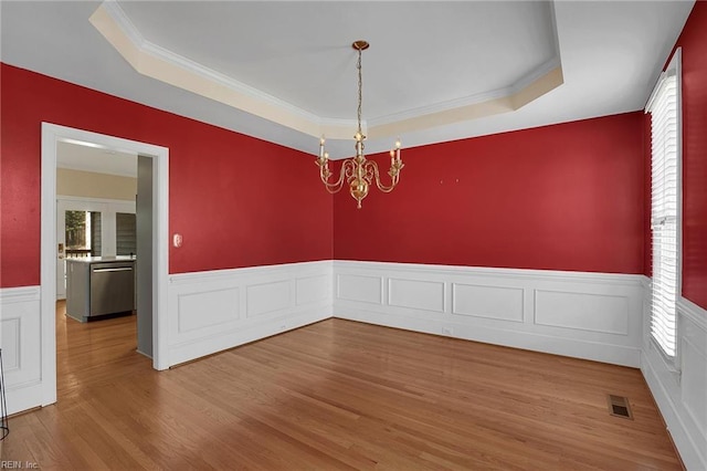 empty room with a tray ceiling, a chandelier, crown molding, and wood-type flooring