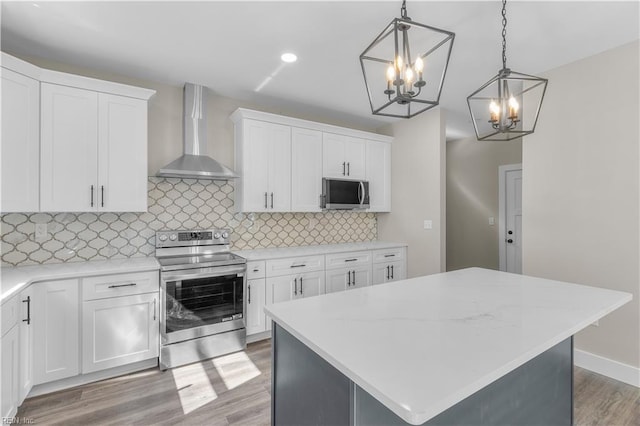 kitchen featuring wall chimney range hood, a kitchen island, white cabinetry, and stainless steel appliances