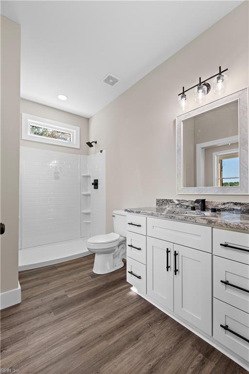 full bath with visible vents, a shower, toilet, wood finished floors, and vanity