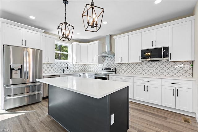 kitchen with stainless steel appliances, light countertops, wall chimney range hood, white cabinetry, and pendant lighting