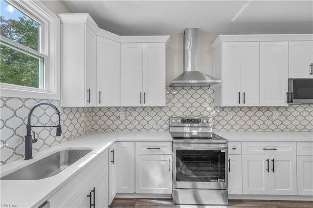 kitchen with wall chimney exhaust hood, white cabinets, and electric stove