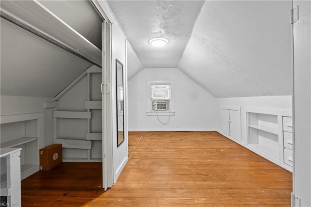 additional living space featuring lofted ceiling, light hardwood / wood-style flooring, a textured ceiling, and built in shelves