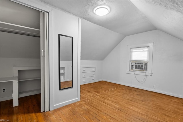 additional living space with wood-type flooring, vaulted ceiling, cooling unit, and a textured ceiling