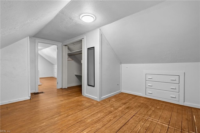 bonus room featuring vaulted ceiling, light hardwood / wood-style flooring, and a textured ceiling