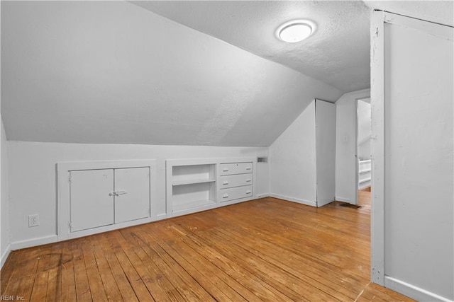 bonus room featuring vaulted ceiling, light hardwood / wood-style flooring, a textured ceiling, and built in shelves