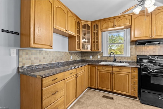 kitchen with sink, backsplash, dark stone counters, ceiling fan, and black gas stove