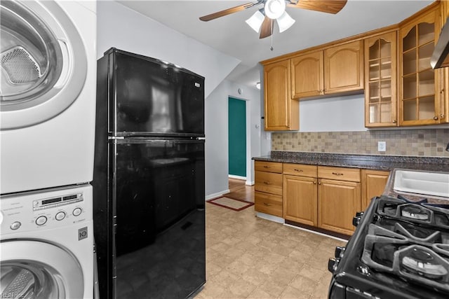 kitchen featuring black refrigerator, sink, stacked washer and clothes dryer, ceiling fan, and gas stove