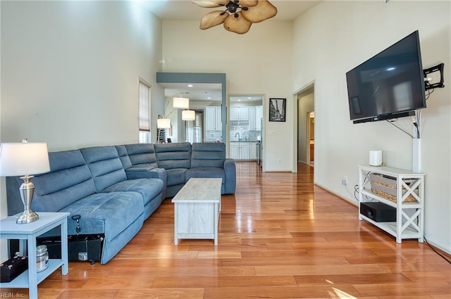 living room with light wood-type flooring, ceiling fan, and a towering ceiling