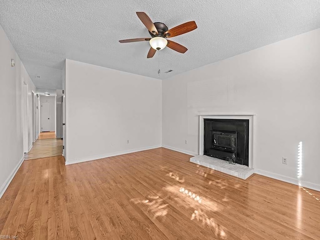 unfurnished living room with a wood stove, light hardwood / wood-style flooring, ceiling fan, and a textured ceiling