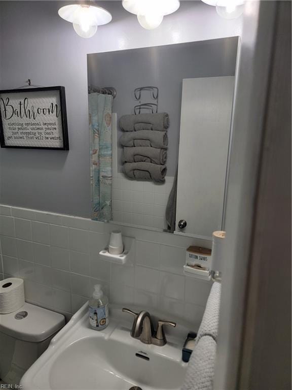 bathroom featuring toilet, sink, and tile walls