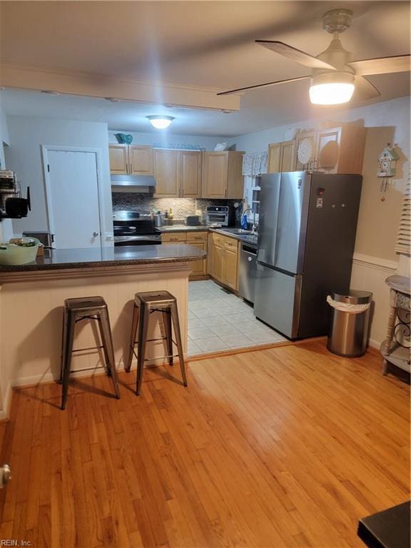 kitchen with a breakfast bar area, light hardwood / wood-style floors, kitchen peninsula, stainless steel appliances, and light brown cabinets