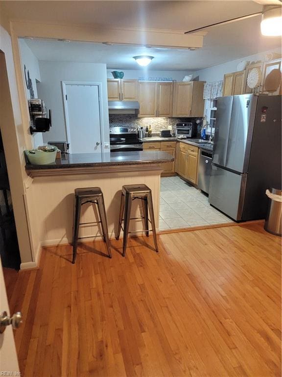 kitchen with a breakfast bar, stainless steel appliances, light wood-type flooring, kitchen peninsula, and light brown cabinets