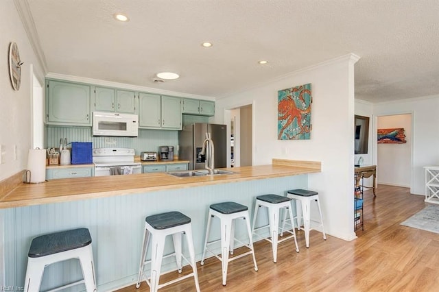 kitchen featuring green cabinetry, kitchen peninsula, white appliances, and a breakfast bar area