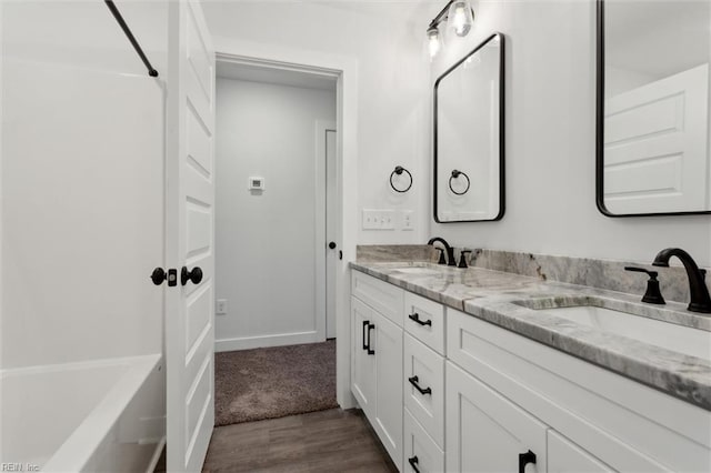 bathroom featuring a sink, a tub, double vanity, and wood finished floors