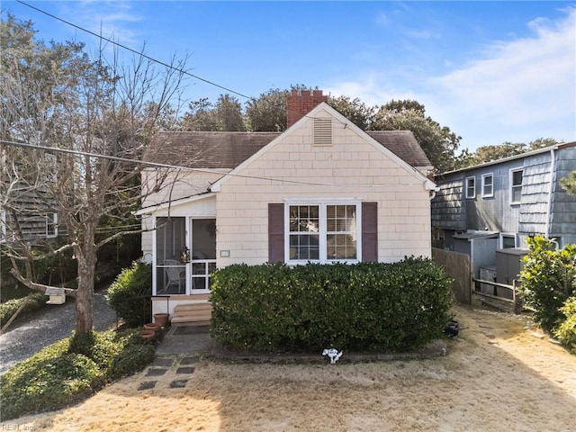 bungalow with a shingled roof, a sunroom, and a chimney