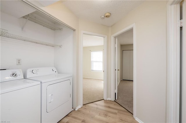 clothes washing area with light wood-type flooring, separate washer and dryer, and a textured ceiling