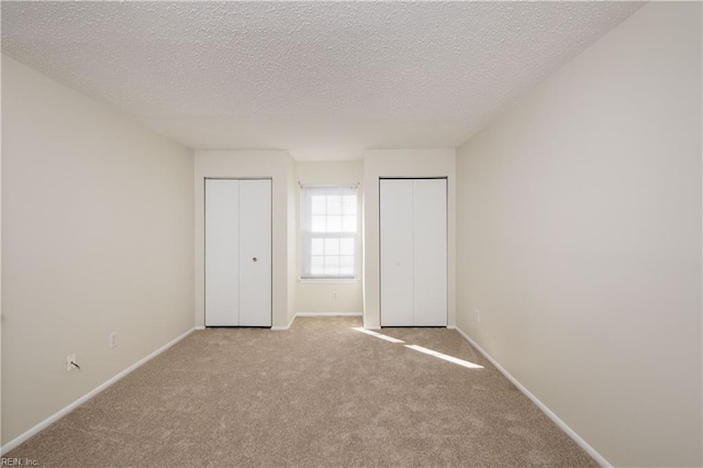 unfurnished bedroom with a textured ceiling, light carpet, and two closets