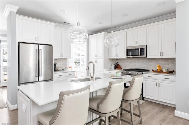 kitchen with stainless steel appliances, light countertops, a center island with sink, and white cabinetry