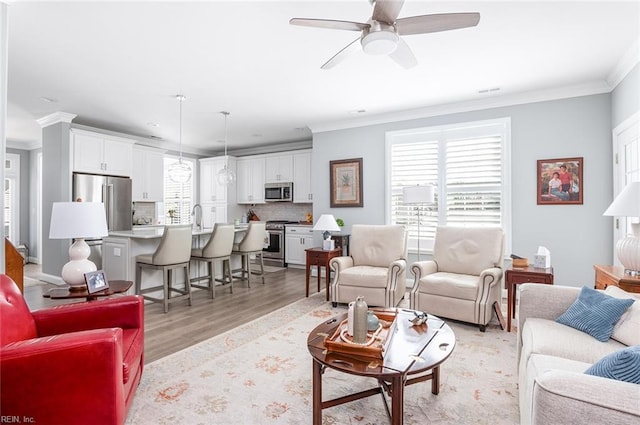 living area with light wood-type flooring, ornamental molding, and a ceiling fan