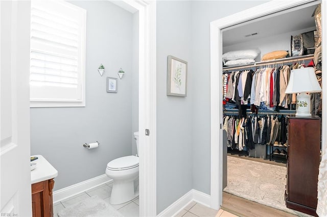 bathroom featuring toilet, baseboards, a walk in closet, and vanity