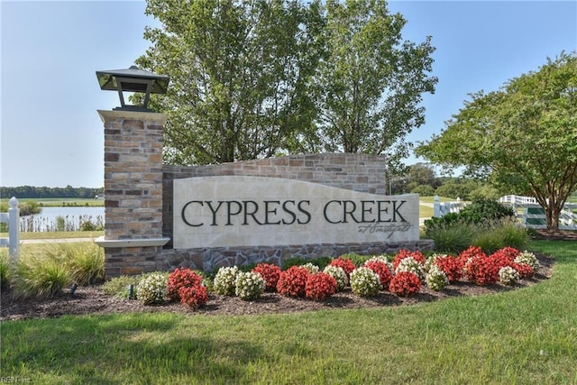 community / neighborhood sign featuring a water view and a lawn