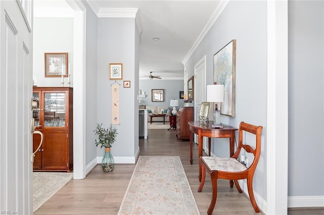 corridor with light wood-style flooring, ornamental molding, and baseboards