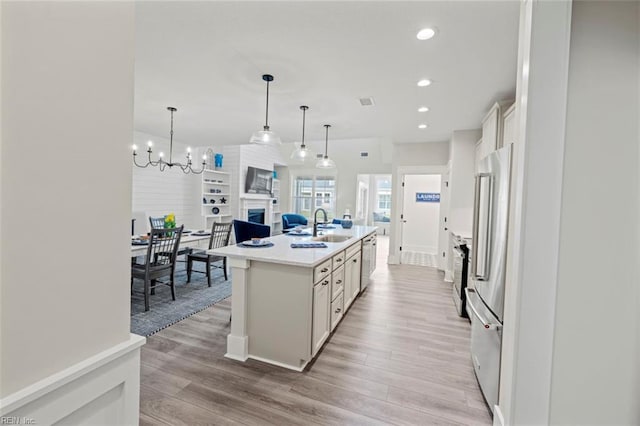 kitchen with white cabinetry, a center island with sink, decorative light fixtures, light hardwood / wood-style floors, and sink