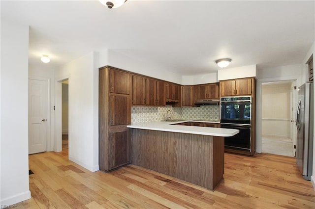 kitchen featuring tasteful backsplash, freestanding refrigerator, a peninsula, light countertops, and light wood-type flooring