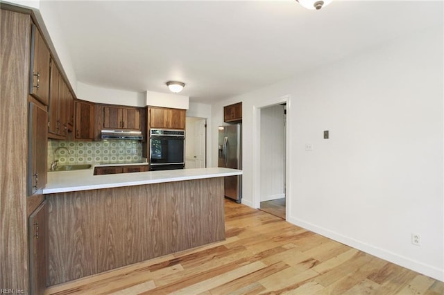 kitchen with under cabinet range hood, a peninsula, light countertops, stainless steel refrigerator with ice dispenser, and backsplash