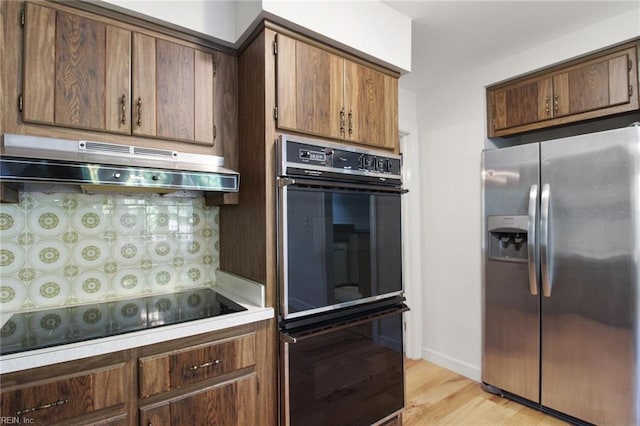 kitchen with black appliances, under cabinet range hood, light countertops, and light wood-style floors